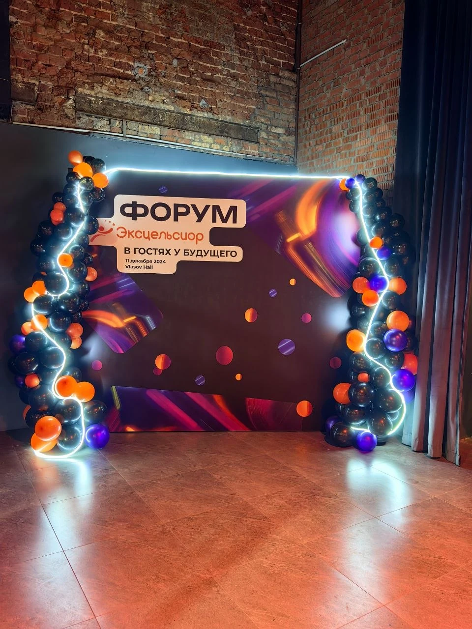 Брендированная фотозона форума с ярким баннером, чёрными, оранжевыми и фиолетовыми шарами и световым контуром